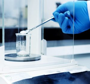 Scientist weighing out a white powder into a beaker on a laboratory balance