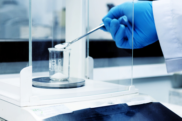 Scientist weighing out a white powder into a beaker on a laboratory balance