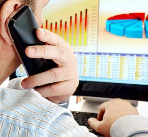 Man on a phone analysing data and charts on computer screen