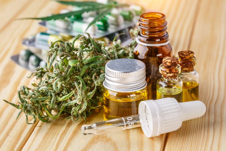 Green leaves of medicinal cannabis with vials of extract oil, tablets in blister packages and a cannbis bud - idea of medicinal cannabis