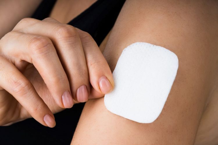 woman applying or removing a microneedle drug patch to her upper arm