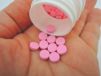 Close up of a hand holding bright pink Warfarin sodium tablets and a white pill bottle - Warfarin sodium is a narrow therapeutic index drug