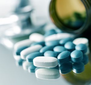 Close up of blue and white tablets spilling out of a medicine bottle onto a table with blurred background - idea of solid form narrow therapeutic index drugs