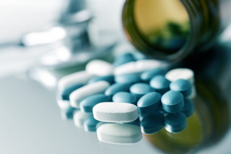 Close up of blue and white tablets spilling out of a medicine bottle onto a table with blurred background - idea of solid form narrow therapeutic index drugs
