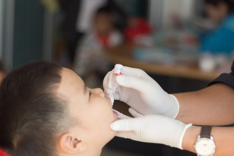 Male Thai child receiving oral polio vaccine from healthcare worker [Credit: frank60 / Shutterstock.com].