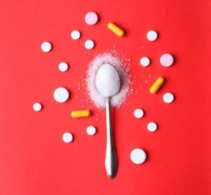 tablets and capsules surrounding an overflowing spoonful of sugar on a red background - idea of paediatric medicines