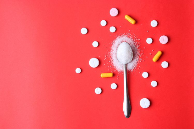 tablets and capsules surrounding an overflowing spoonful of sugar on a red background - idea of paediatric medicines