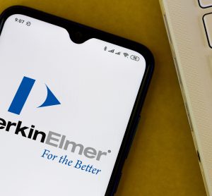 Phone screen displaying PerkinElmer logo next to a laptop keyboard [Credit: rafapress / Shutterstock.com].