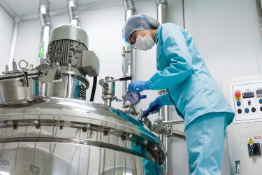Factory worker inspecting an aluminium tank in a pharmaceutical production facility