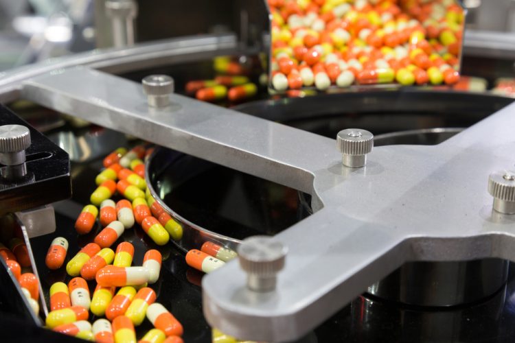 Bright orange and yellow capsules on a production line at a pharmaceutical factory - idea of pharma manufacturing