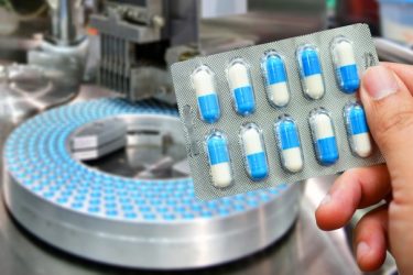 Hand holding blue capsule pack at medicine pill production line