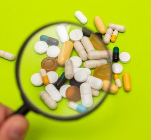 pills, tablets and capsules of various shapes, sizes and colours under a magnifying glass - idea of pharmacovigilance or drug safety