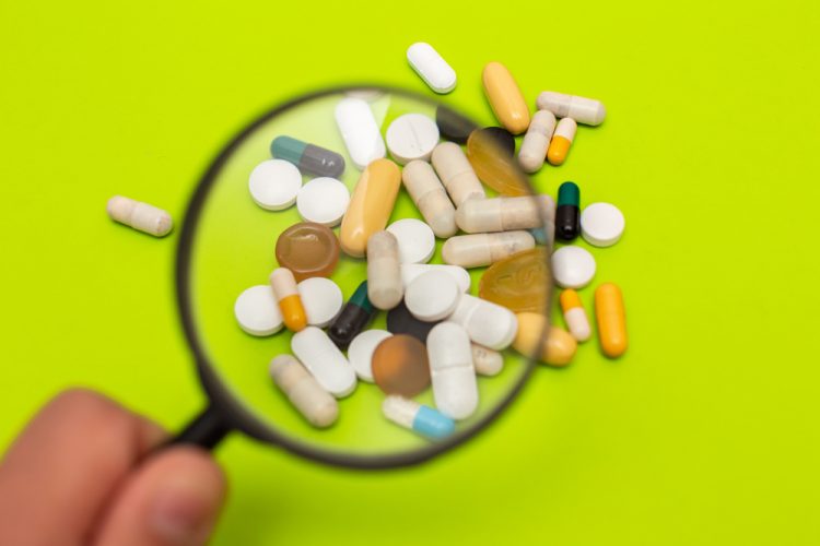 pills, tablets and capsules of various shapes, sizes and colours under a magnifying glass - idea of pharmacovigilance or drug safety