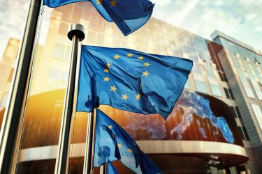 EU flags (blue with central circle of yellow stars) waving in front of European Parliament building. Brussels, Belgium