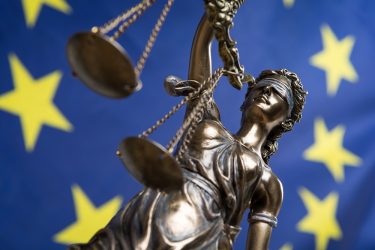 statue of lady justice holding scales in front of EU flag
