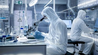 In a Secure High Level Laboratory Scientists in a Coverall Conducting a Research. Biologist Adjusts Samples in a  Petri Dish with Pincers and Examines Them Under Microscope.