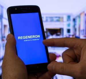 Phone with regeneron logo on it in front of blurred laboratory background [Credit: adrianosiker.com/Shutterstock.com].