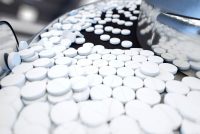 Pharmaceutical manufacturing - stainless steel machine with white circular pills flowing down a conveyor