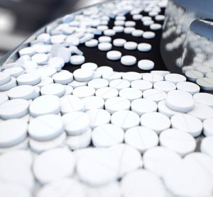 Pharmaceutical manufacturing - stainless steel machine with white circular pills flowing down a conveyor