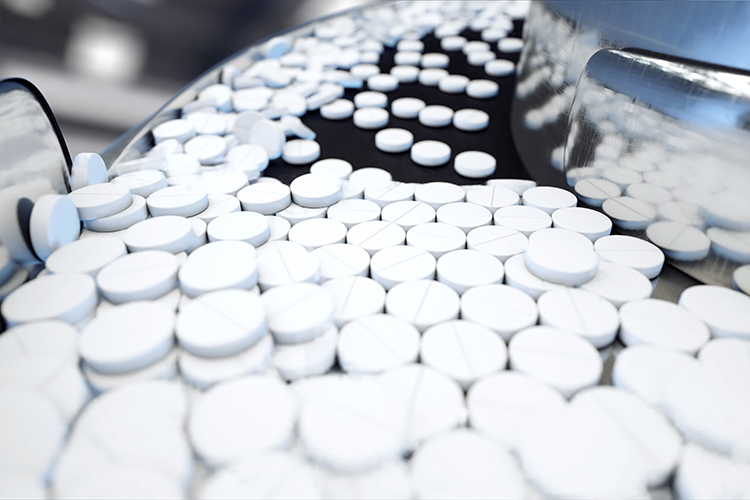 Pharmaceutical manufacturing - stainless steel machine with white circular pills flowing down a conveyor