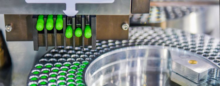 green pharmaceutical capsules being released from a stainless steel machine