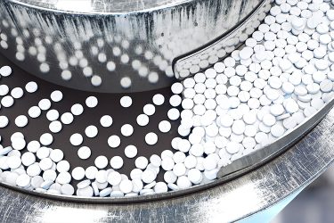 Pharmaceutical manufacturing - stainless steel machine with white circular pills flowing down a conveyor