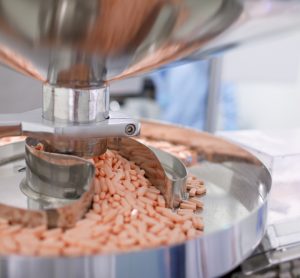 Light orange tablets being released from a machine onto a tray at a manufacturing facility