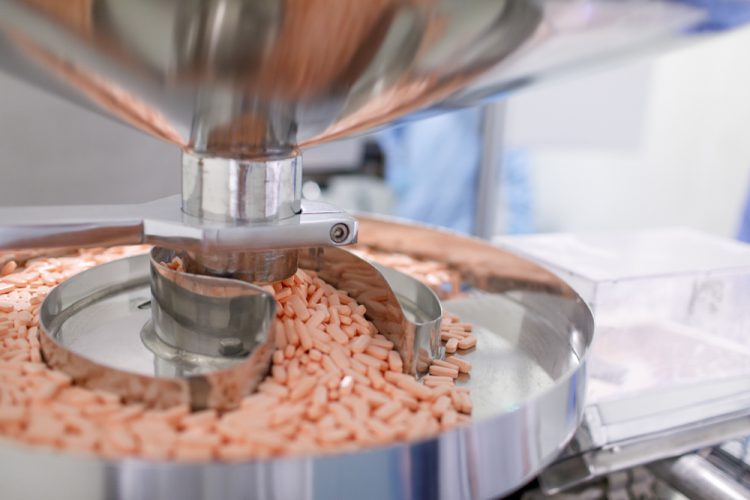 Light orange tablets being released from a machine onto a tray at a manufacturing facility
