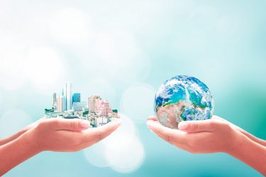 Two hands, one on left holding a cartoon city, the other holding a globe - idea of environmental and social goals