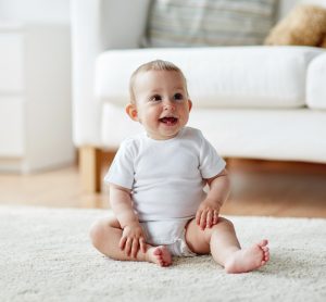 happy little baby boy or girl sitting on floor at home