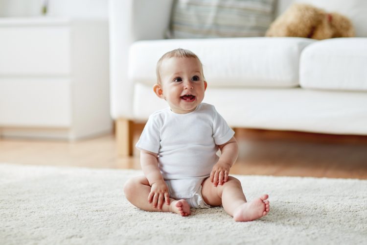 happy little baby boy or girl sitting on floor at home