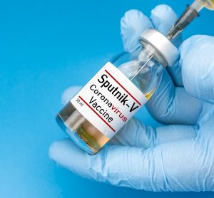 Glove hands holding a vial labelled 'SPUTNIK V CORONAVIRUS VACCINE' and drawing from it with a syringe