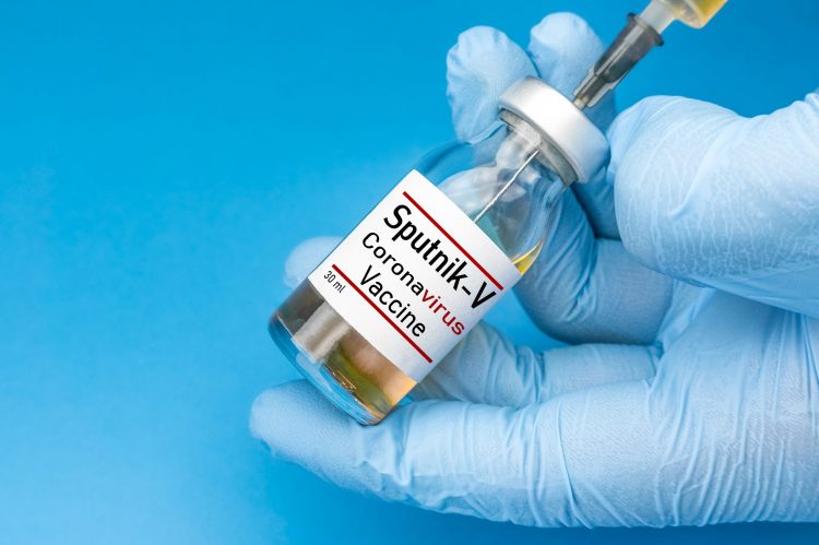 Glove hands holding a vial labelled 'SPUTNIK V CORONAVIRUS VACCINE' and drawing from it with a syringe
