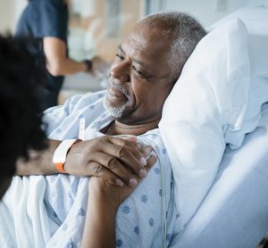 man in a hospital bed holding hand of person sat next to them