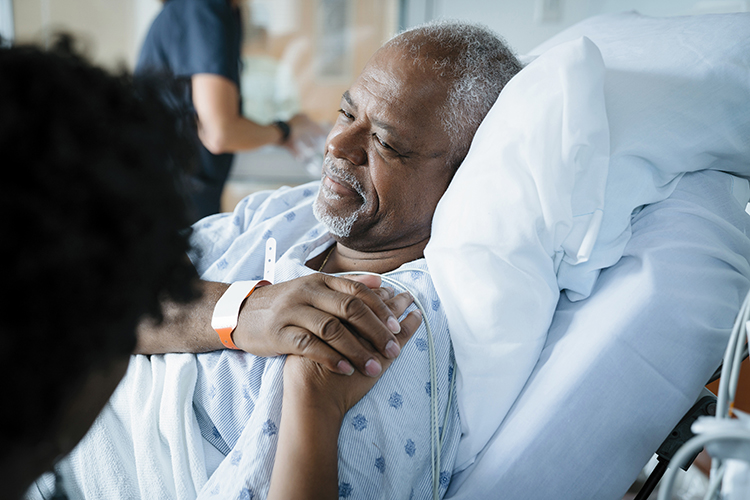 man in a hospital bed holding hand of person sat next to them