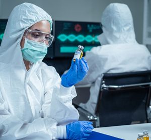 Laboratory researcher in cleanroom garments looking at a pharmaceutical vial