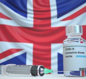 Vial labelled 'COVID-19 Vaccine' with a syringe in front of a union jack flag