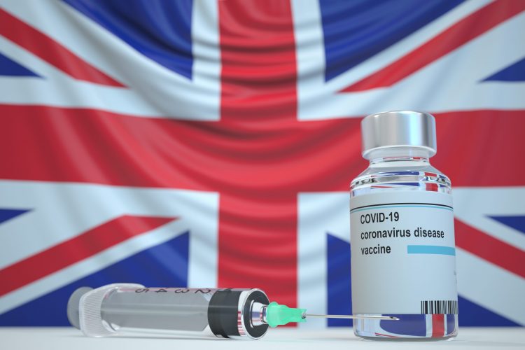 Vial labelled 'COVID-19 Vaccine' with a syringe in front of a union jack flag