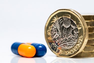 two blue and orange capsules next to a stack of pound coins - idea of funding for life sciences/medicine