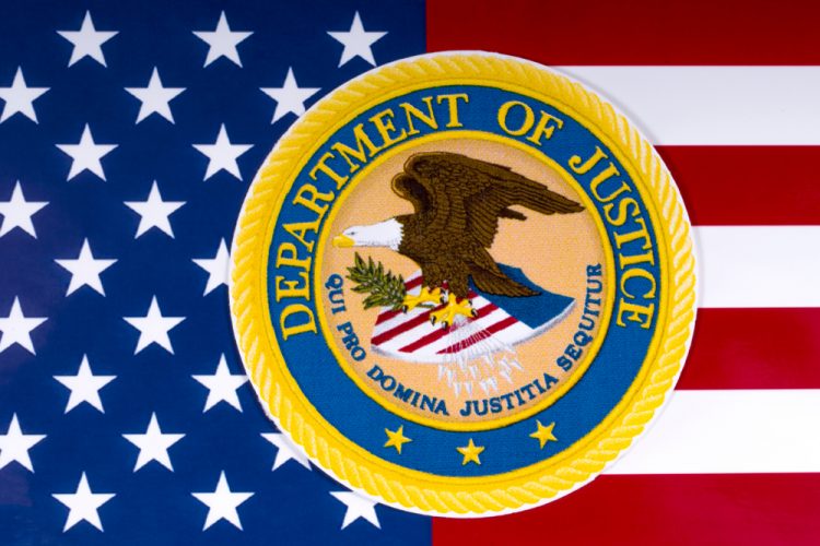 US Department of Justice logo on top of an American Flag [Credit: US-Department-of-Justice].