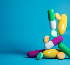 Various tablets and capsules of different colours, shapes and sizes dropping from above onto a flat surface on a blue background