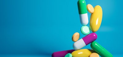 Various tablets and capsules of different colours, shapes and sizes dropping from above onto a flat surface on a blue background