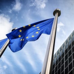 European Union flag (blue with a central circle of yellow stars) on a flag post