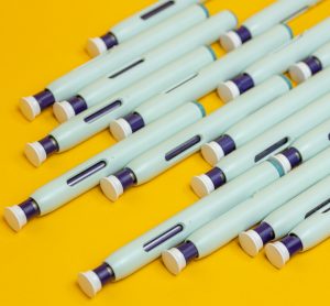 Slanted grouping of self application syringe pens on seamless yellow background.