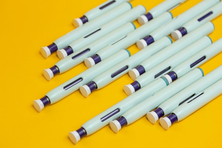 Slanted grouping of self application syringe pens on seamless yellow background.