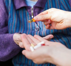 Person handing an elderly man a handful of medications