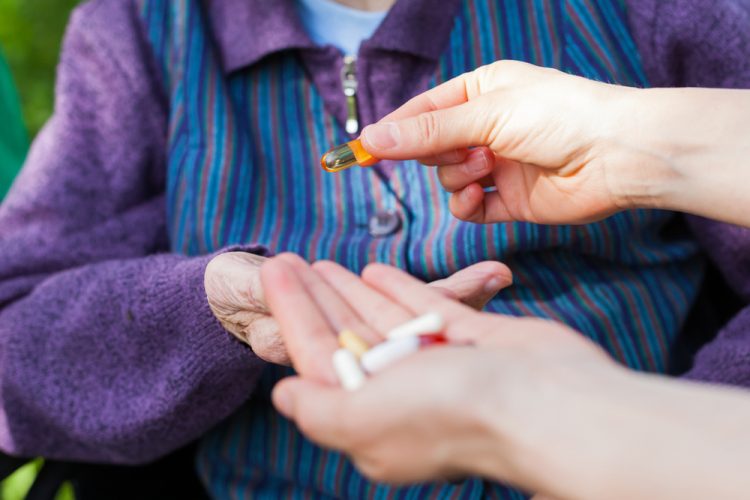 Person handing an elderly man a handful of medications