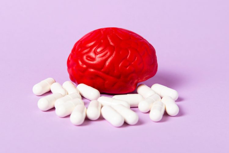 Red brain on a pink background with white pills - idea of antipsychotics or pharmaceuticals targeting mental disorders