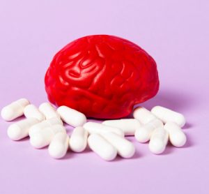 Red brain on a pink background with white pills - idea of antipsychotics or pharmaceuticals targeting mental disorders