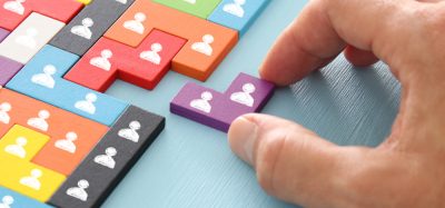 close up of person's hand sliding a wooden puzzle block with people icons on it into a space in a larger puzzle - idea of appointments or recruitment